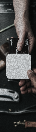 A hand holding two credit cards, one Visa, near a white wireless card reader held by another hand.