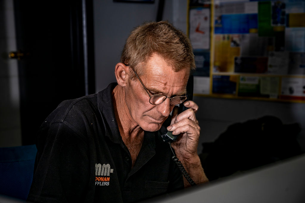 Man with glasses speaking on a corded telephone in a dimly lit office.