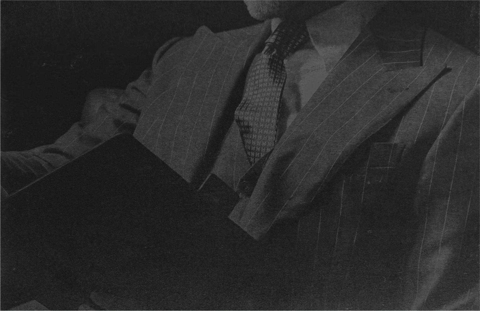 Black and white close-up of a man in a pinstripe suit and patterned tie holding a book.