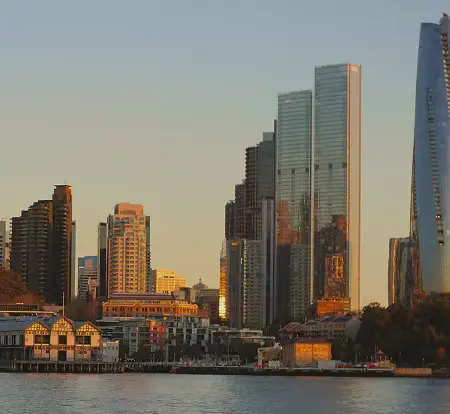 City skyline with modern glass skyscrapers and older low-rise buildings along a waterfront at sunset.