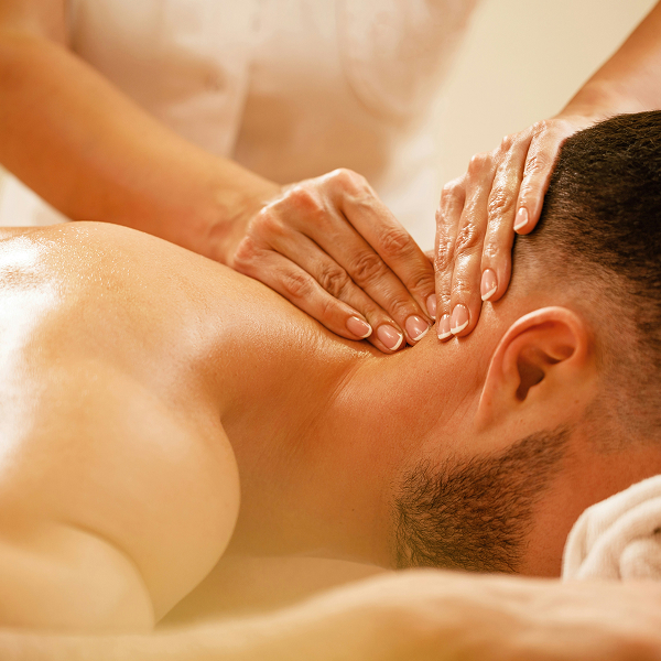 Therapist giving a neck and shoulder massage to a man lying face down on a towel.