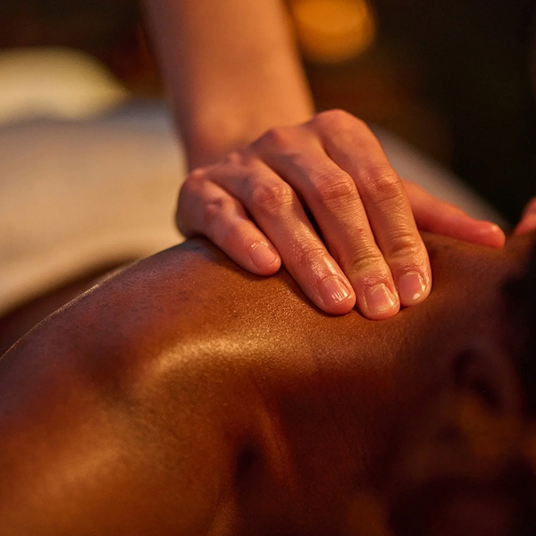 Close-up of a hand giving a deep tissue massage on a person's shoulder under warm light.