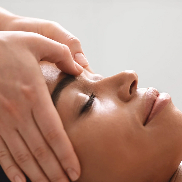 Close-up of a person receiving a gentle facial massage with closed eyes and relaxed expression.