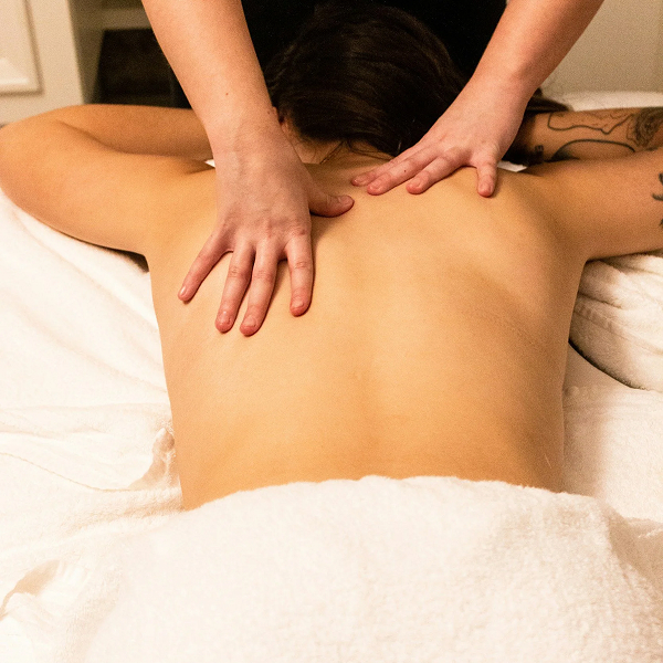Person receiving a back massage on a white towel-covered table with tattooed arm visible.