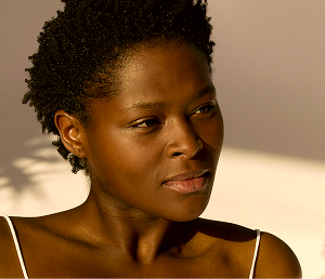 Portrait of a woman with natural short curly hair looking to the side in warm sunlight.