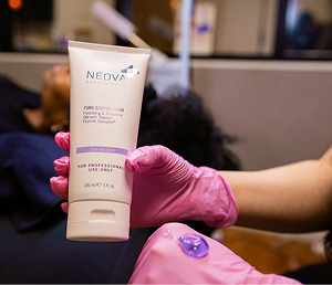 Gloved hand holding Neova skin therapy tube labeled for professional use only in a spa setting.