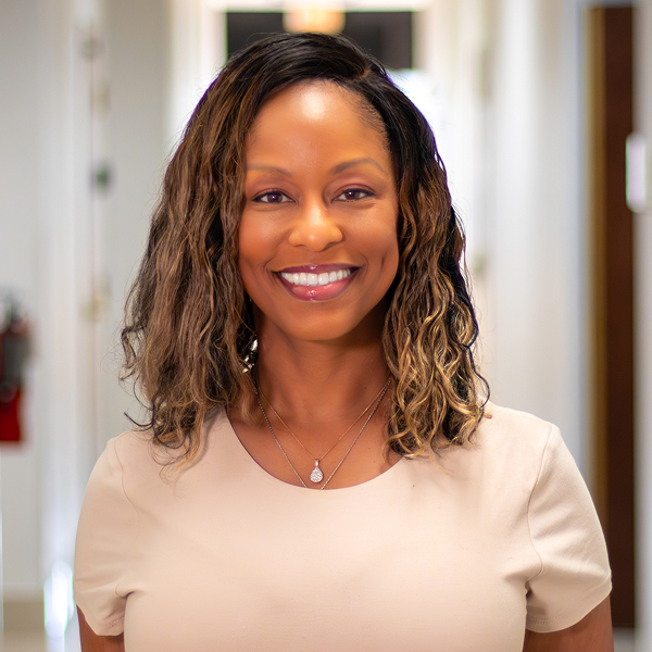 Smiling woman with curled hair wearing a white shirt against a gray background.