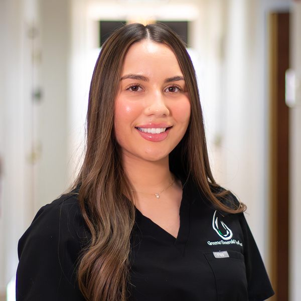 Smiling woman with long brown hair wearing a black uniform in a brightly lit hallway.