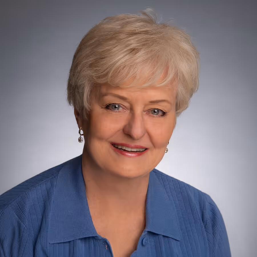 Smiling older woman with short light blonde hair wearing a blue collared sweater.
