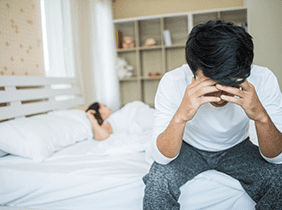 Man smiling while unpacking a small white box from a cardboard box in a warmly lit living room.