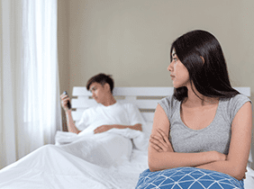 Man smiling while unpacking a small white box from a cardboard box in a warmly lit living room.