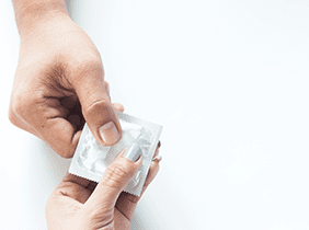 Man smiling while unpacking a small white box from a cardboard box in a warmly lit living room.