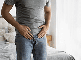Man smiling while unpacking a small white box from a cardboard box in a warmly lit living room.