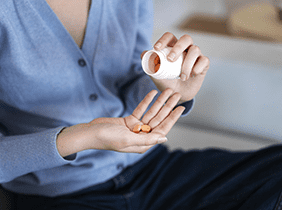 Man smiling while unpacking a small white box from a cardboard box in a warmly lit living room.