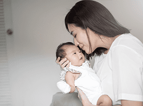 Man smiling while unpacking a small white box from a cardboard box in a warmly lit living room.