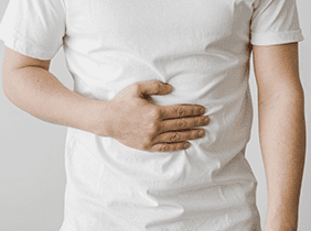 Man smiling while unpacking a small white box from a cardboard box in a warmly lit living room.