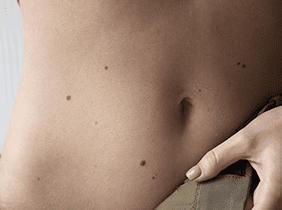 Man smiling while unpacking a small white box from a cardboard box in a warmly lit living room.