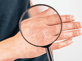 Man smiling while unpacking a small white box from a cardboard box in a warmly lit living room.