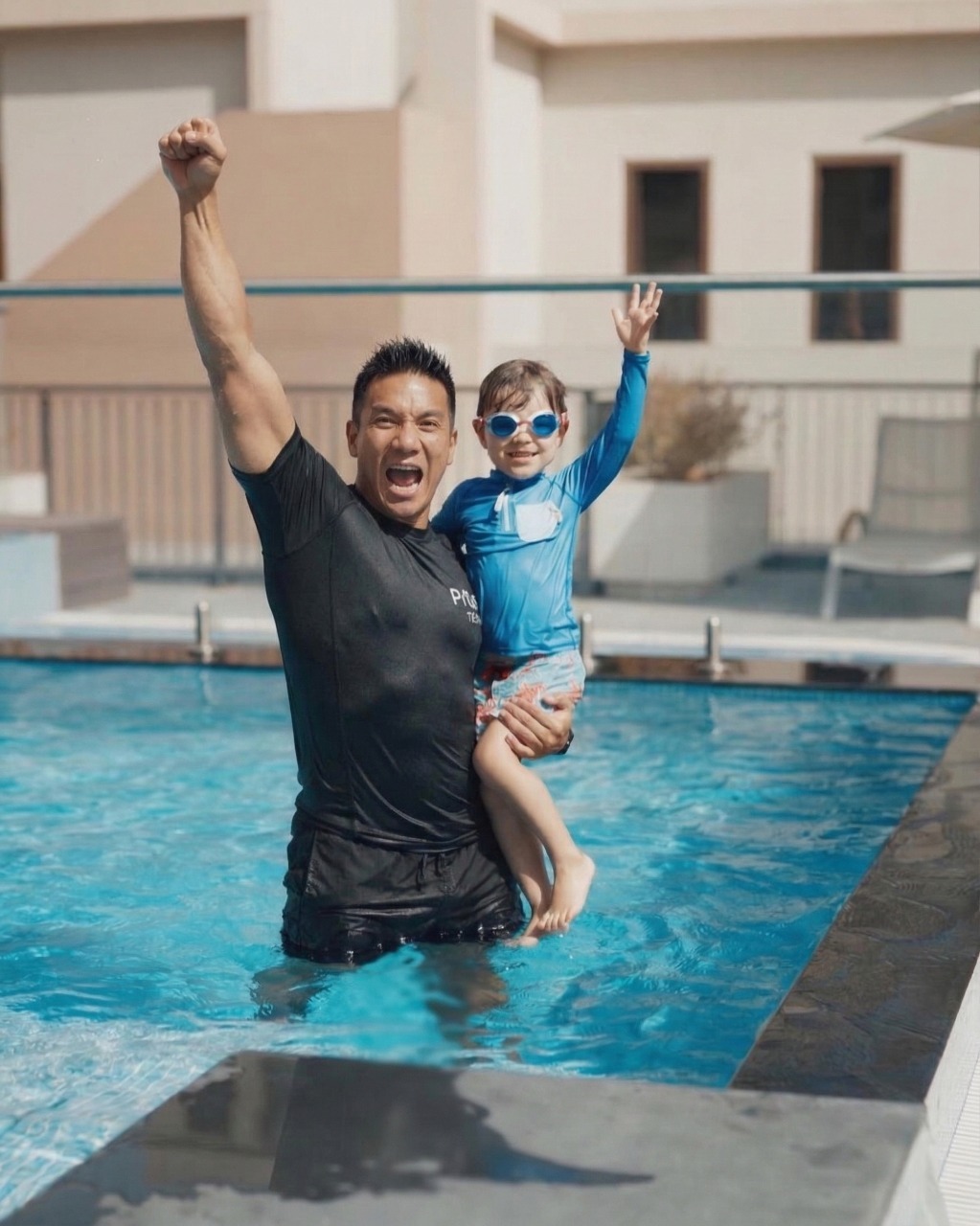 Certified swim coach in Swim Class Singapore uniform celebrating with a toddler in blue swimwear after a successful baby swimming lesson.