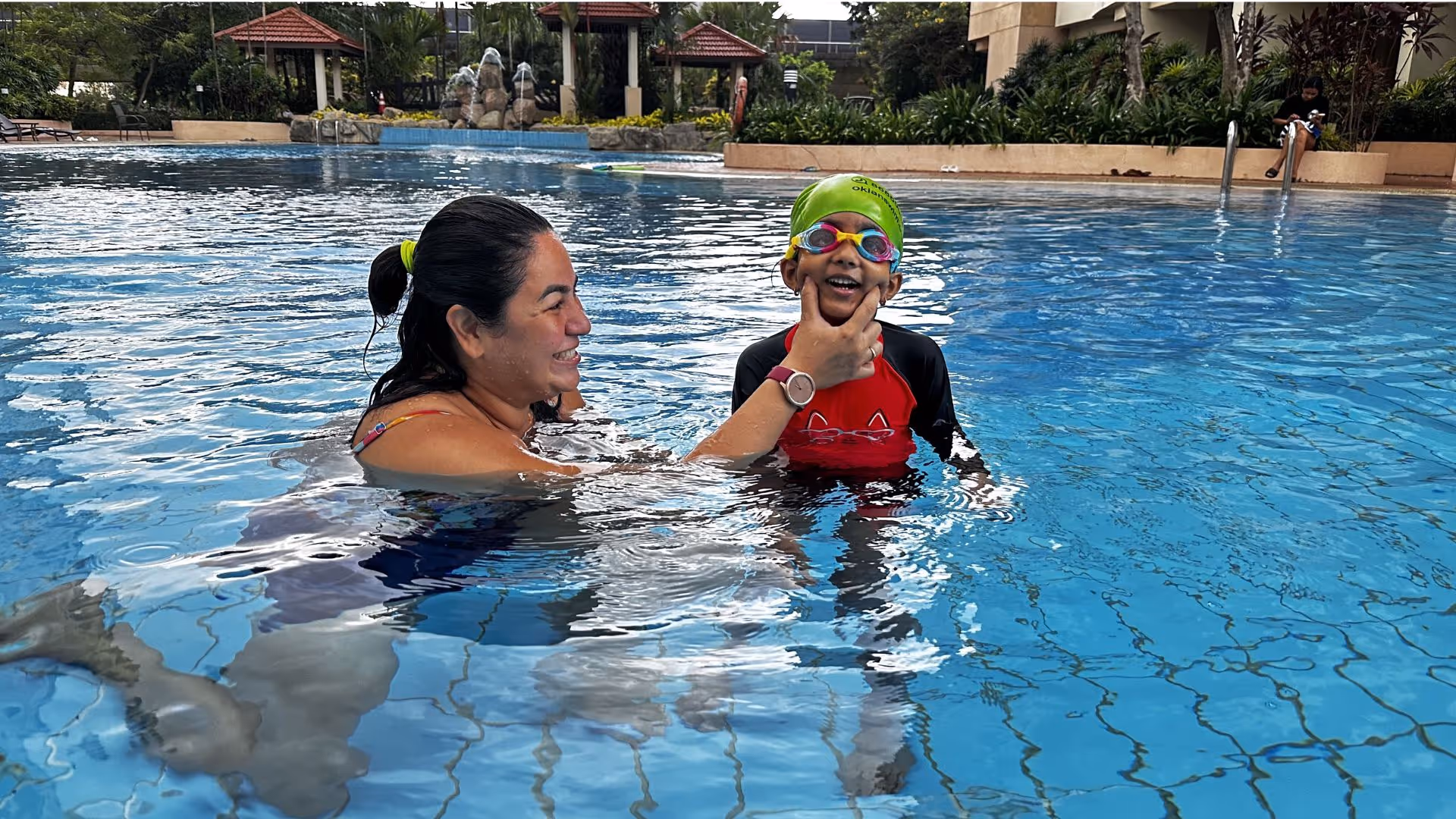 Friendly swim coach teaching a child the foundations of swimming in a Singapore pool, both smiling and having fun
