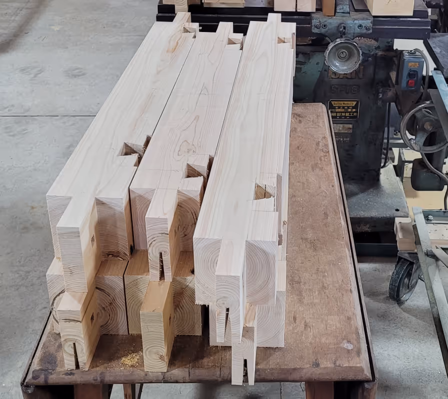 Stack of precisely cut wooden beams with interlocking joints on a workbench in a woodworking shop.