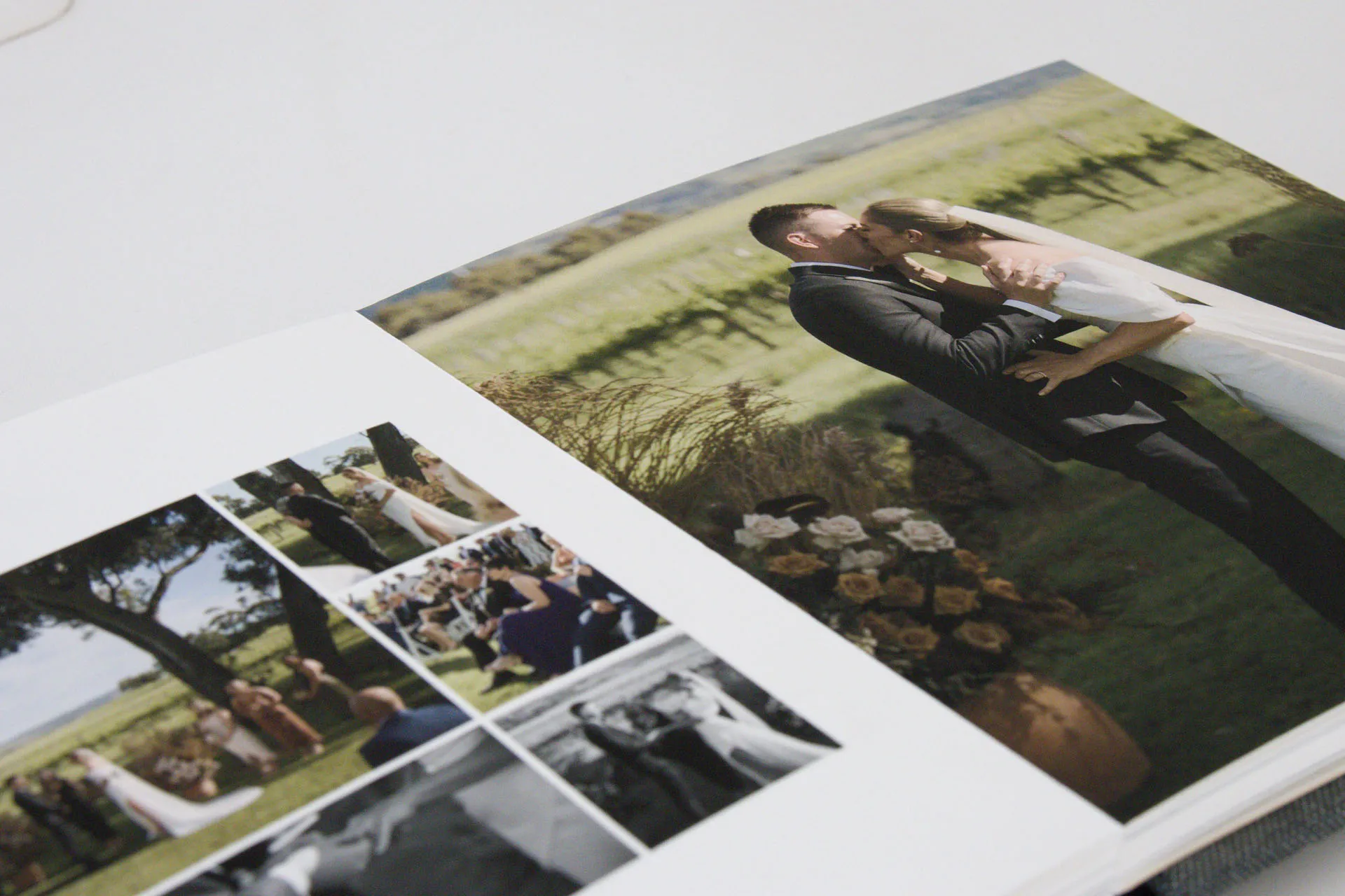 Open wedding photo album showing a couple kissing outdoors and smaller images of the ceremony with guests.