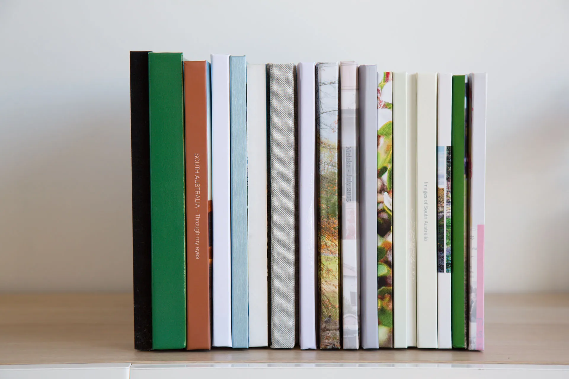 A row of various hardcover and softcover books standing vertically on a wooden surface against a plain white background.