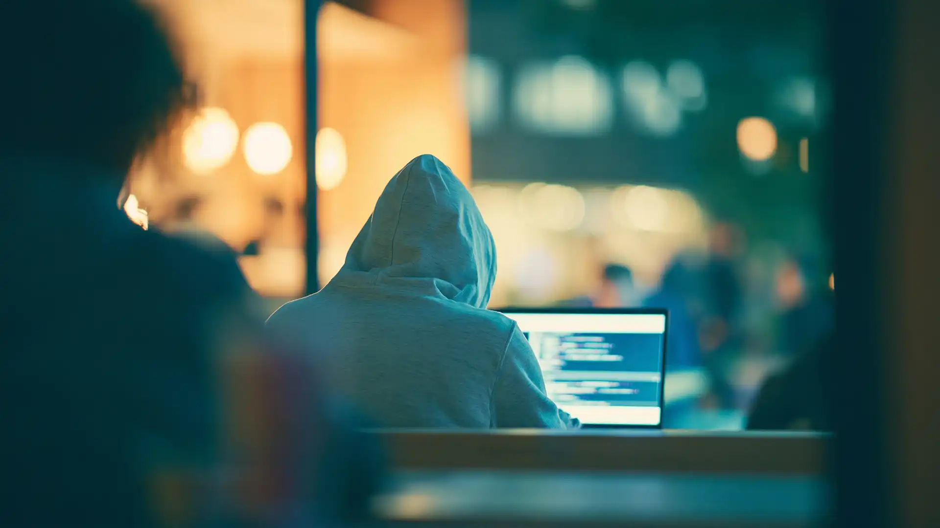Person in a hoodie working on a laptop in an urban modern cafe