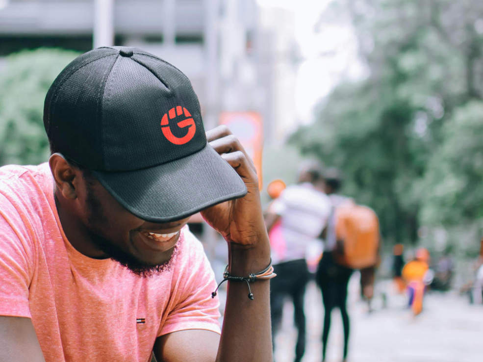 Man talking on phone and smiling wearing a hat with orange GAMESQ "G" logo