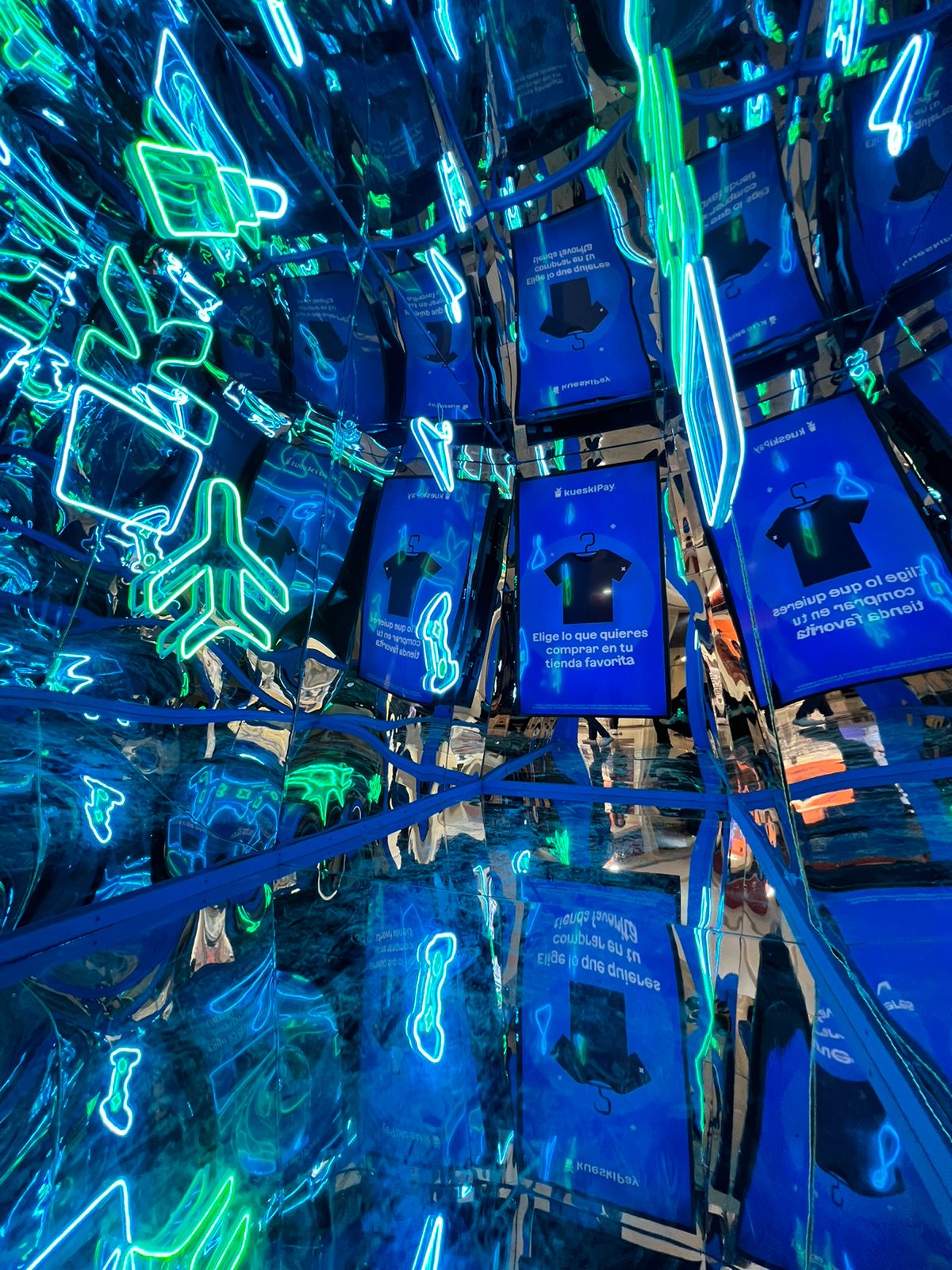 Mirrored room with neon blue and green icons and multiple reflections of blue screens showing a black shirt.