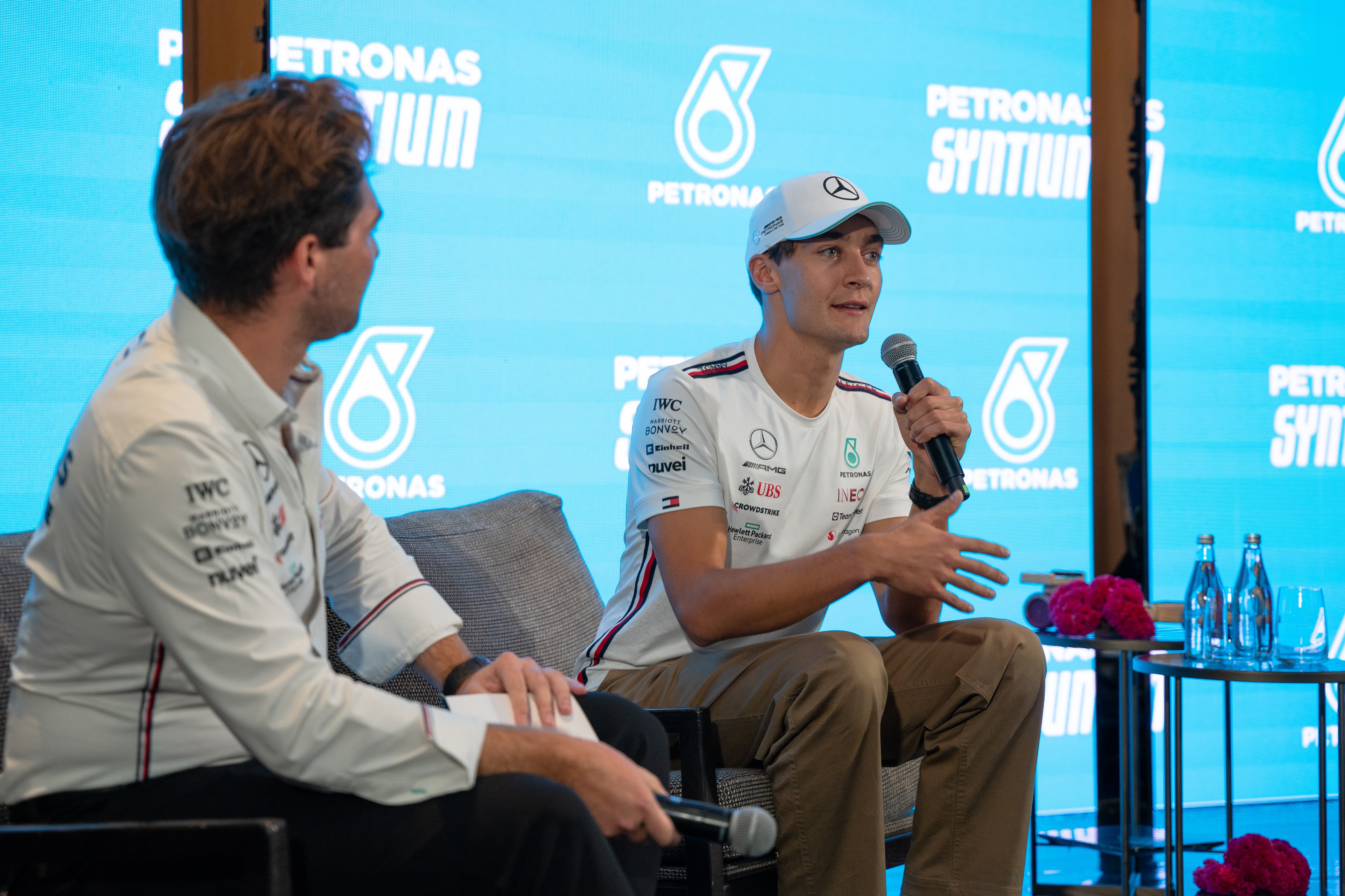 Two men in Mercedes-AMG Petronas team shirts having a discussion during a press event.