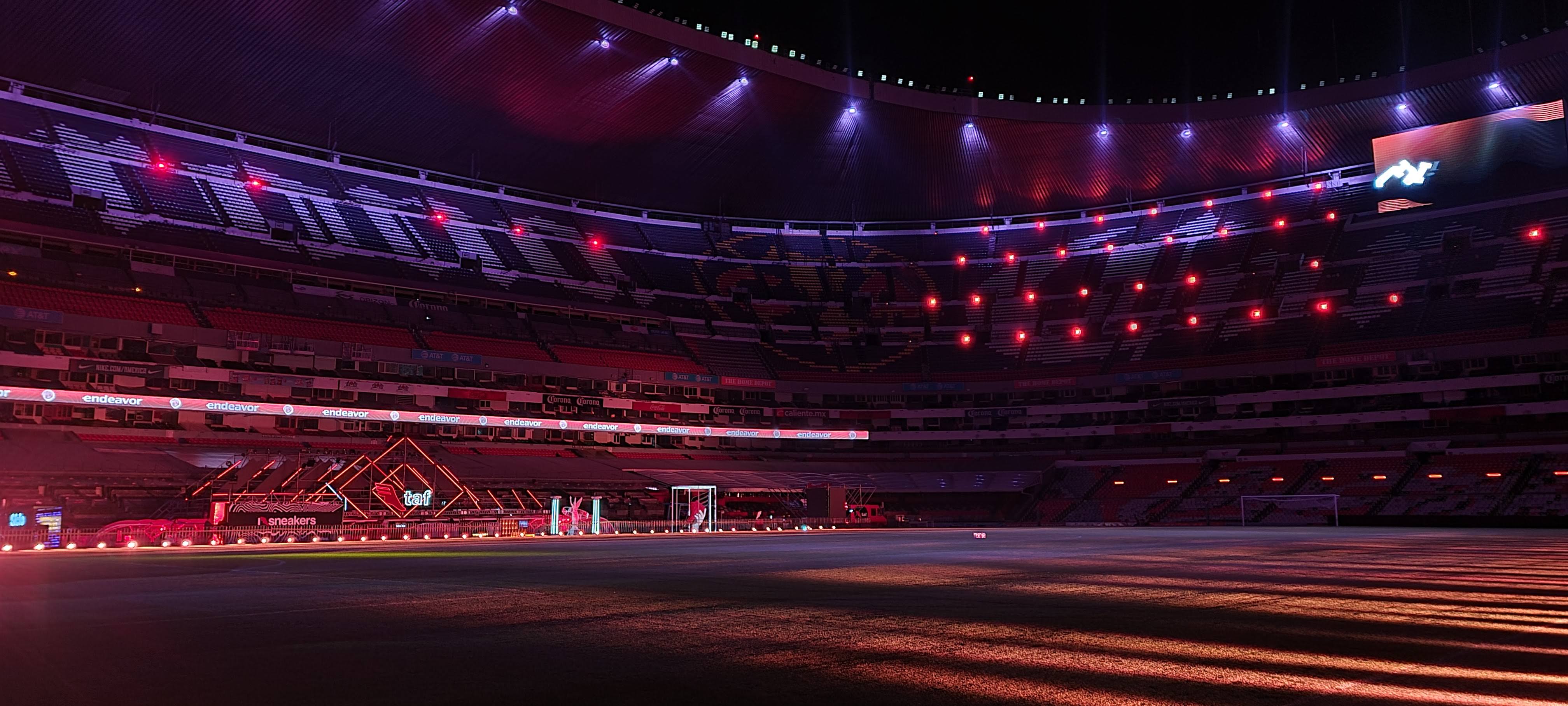 Empty stadium at night with red and purple lighting and a stage setup on the field.