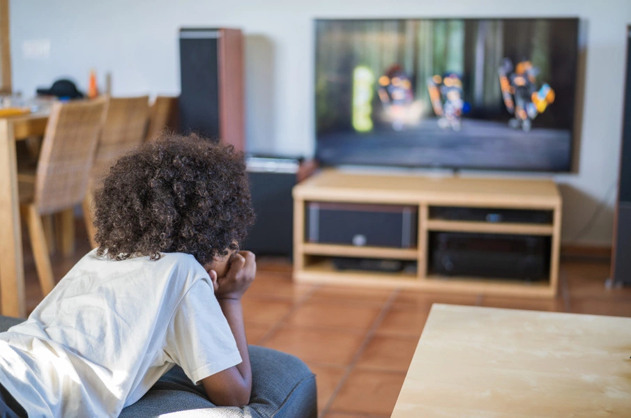 Imagen de un niño viendo dibujos animados en la televisión mientras está acostado en la cama.