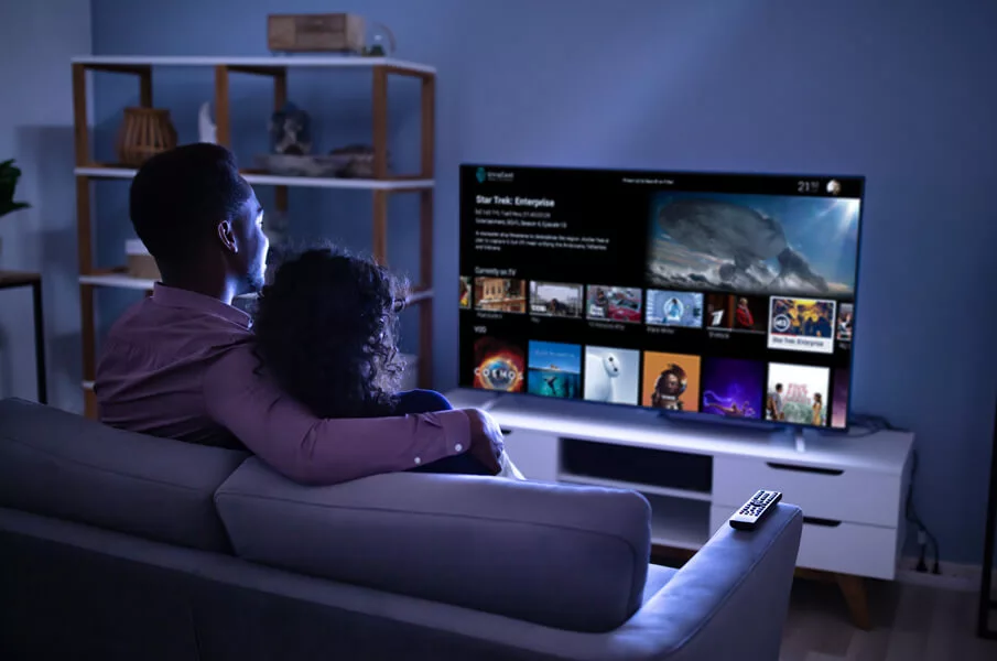 Imagen de una pareja sentada en un sofá y navegando por los canales de un televisor.