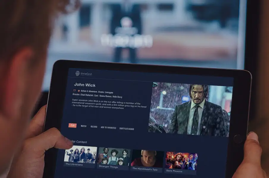 Imagen de un hombre que sostiene una tableta en sus manos con el logotipo de Uniqcast en la esquina superior izquierda y busca una película.