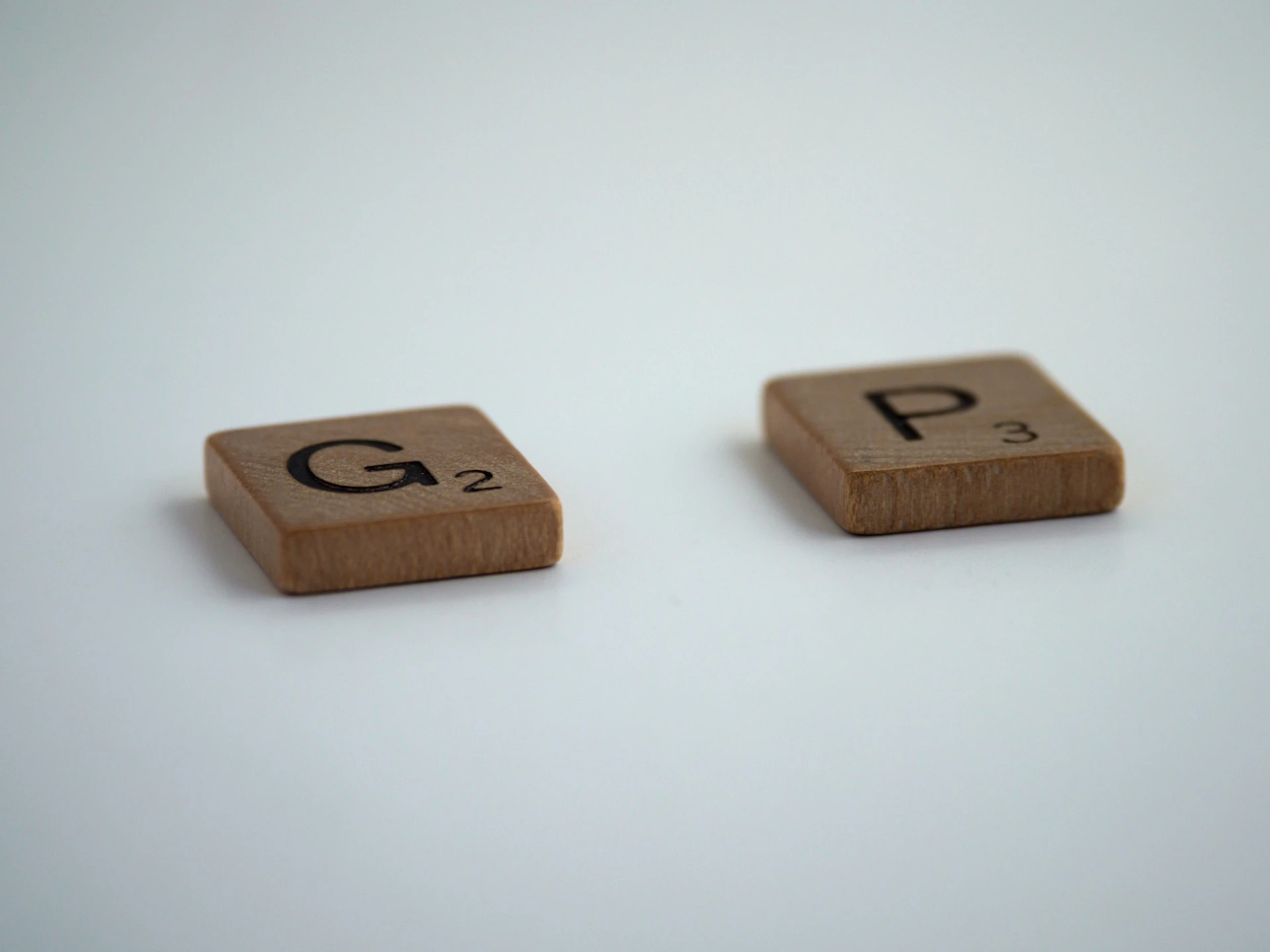Fichas de madera con las letras G y P de un juego de Scrabble a las que les falta la A en el centro.
