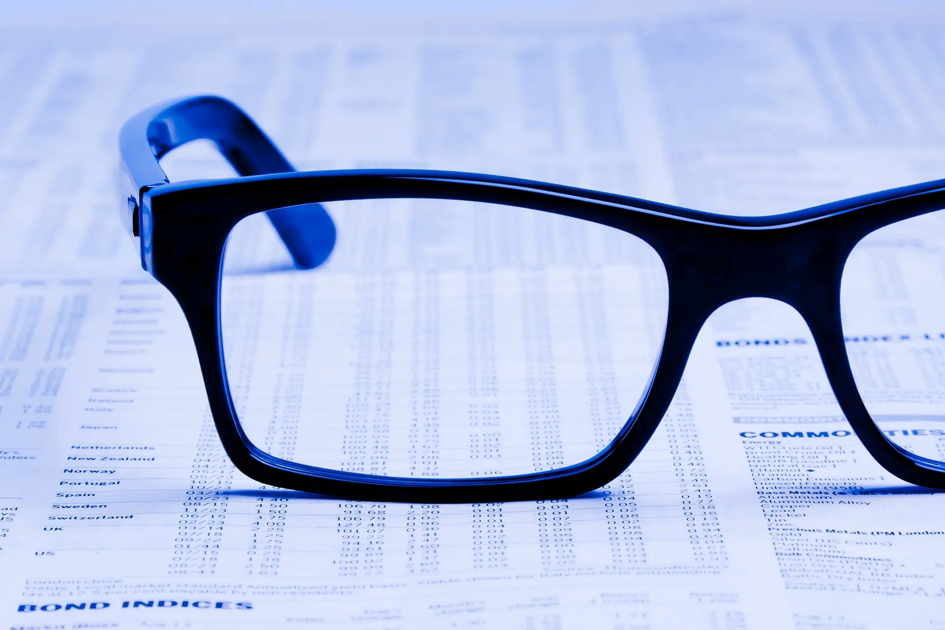 A pair of eyeglasses with dark frames placed on top of a newspaper featuring financial data and stock market information.