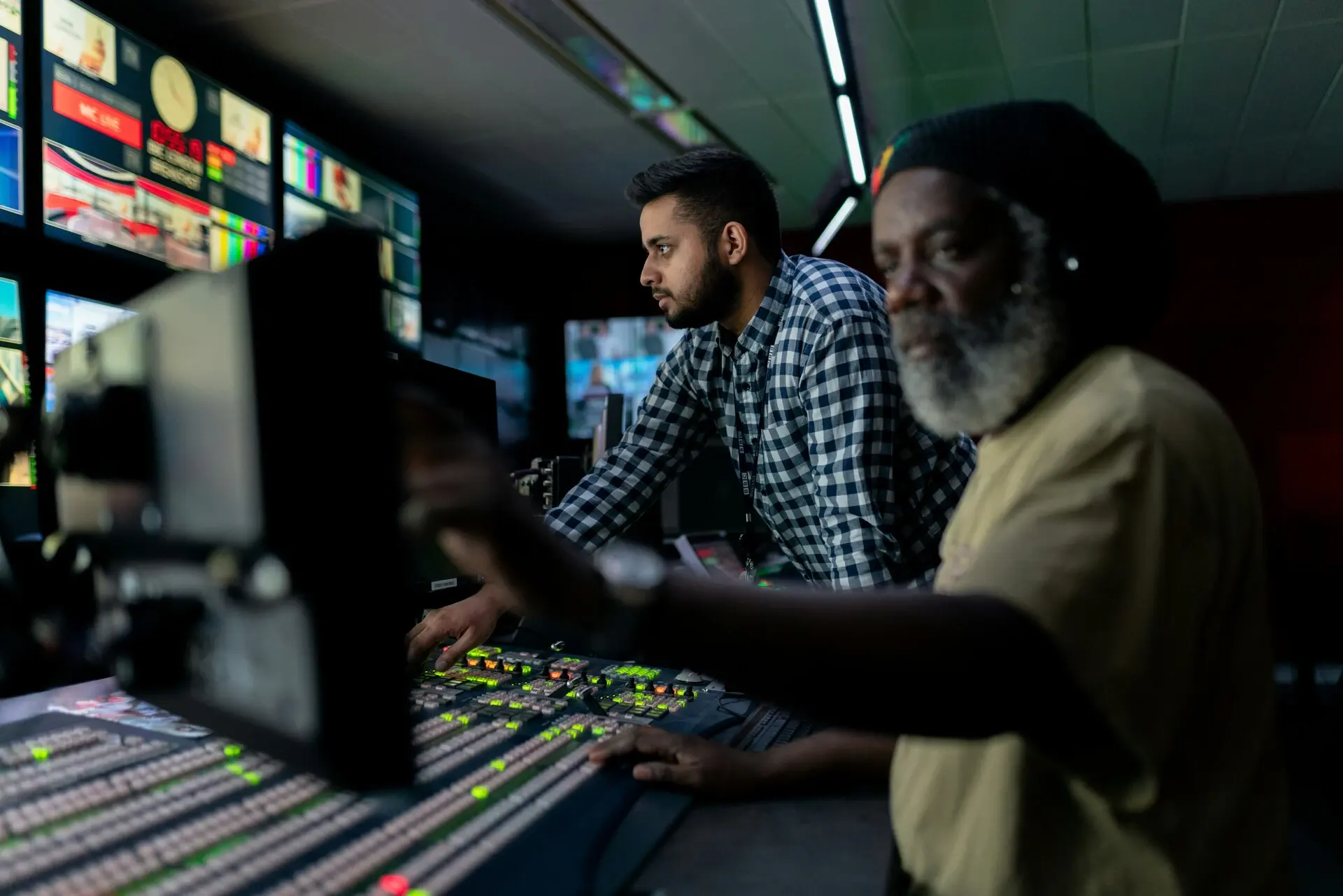 Two people operate a control panel in a dimly lit production studio, focusing intently on their ott platform post-migration.