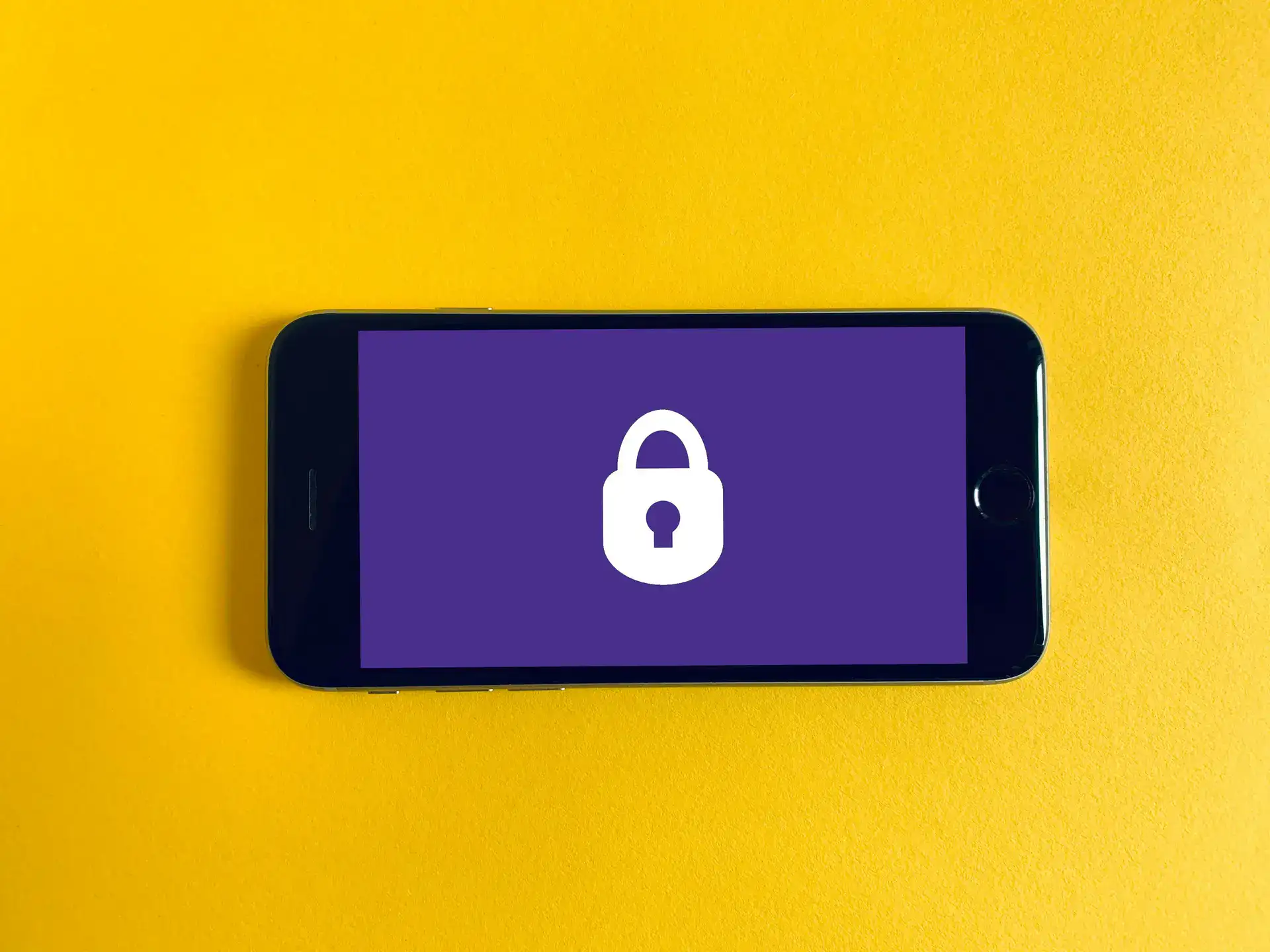 Un smartphone tumbado sobre una superficie amarilla que muestra en su pantalla el icono de un candado, símbolo de la seguridad digital.