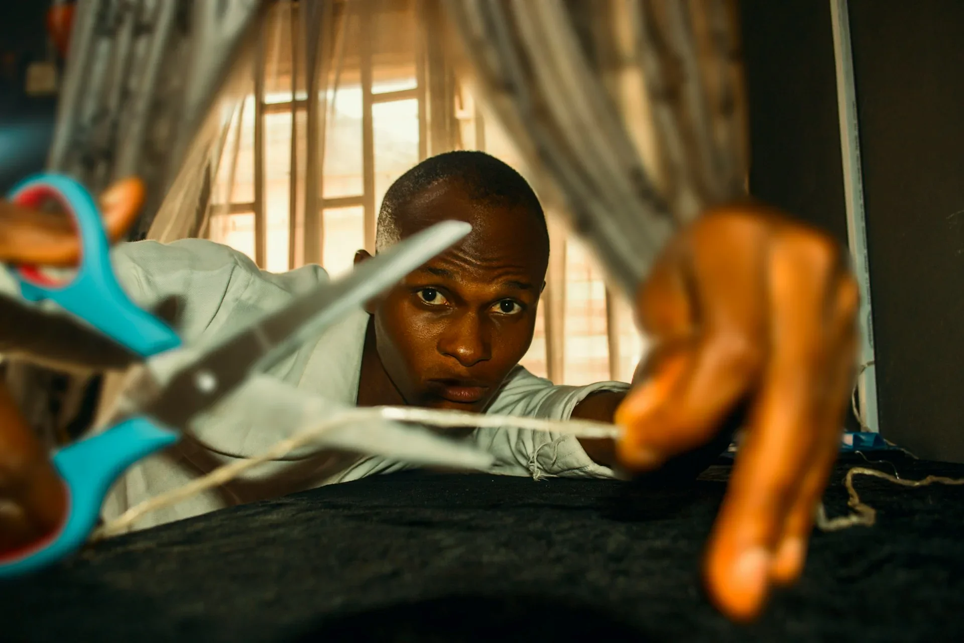 Un sastre con unas tijeras parece cortar una cuerda o un hilo, en un interior con cortinas al fondo.