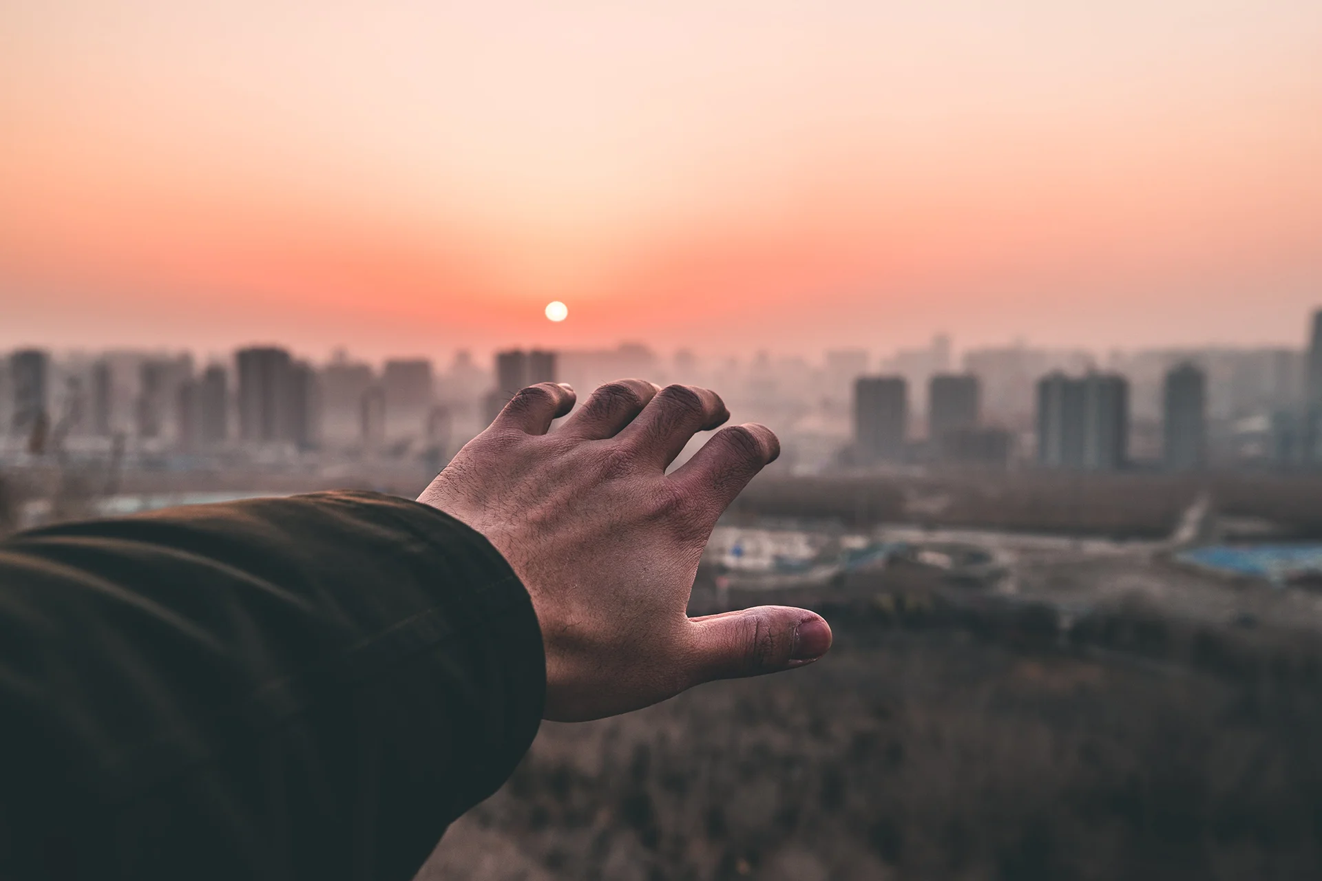 una mano tendida hacia la ciudad en la lejanía al atardecer