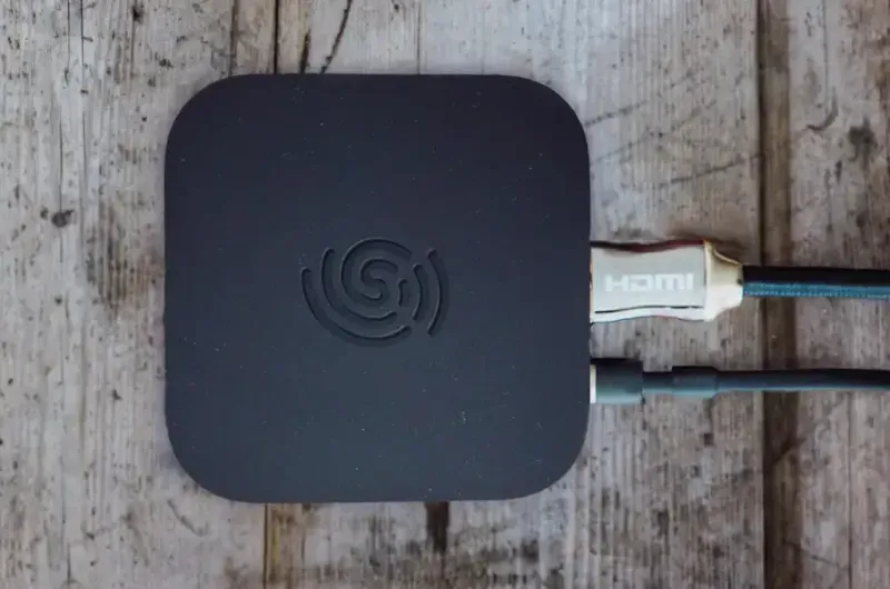 Dispositivo STB negro híbrido sobre una superficie de madera con cables HDMI y de alimentación conectados a él en el lado derecho attac