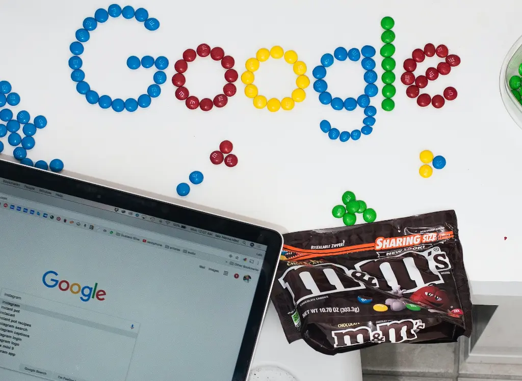 Una mesa con una bolsa de caramelos M&M ordenados para deletrear "Google" y un portátil con la búsqueda de Google abierta.
