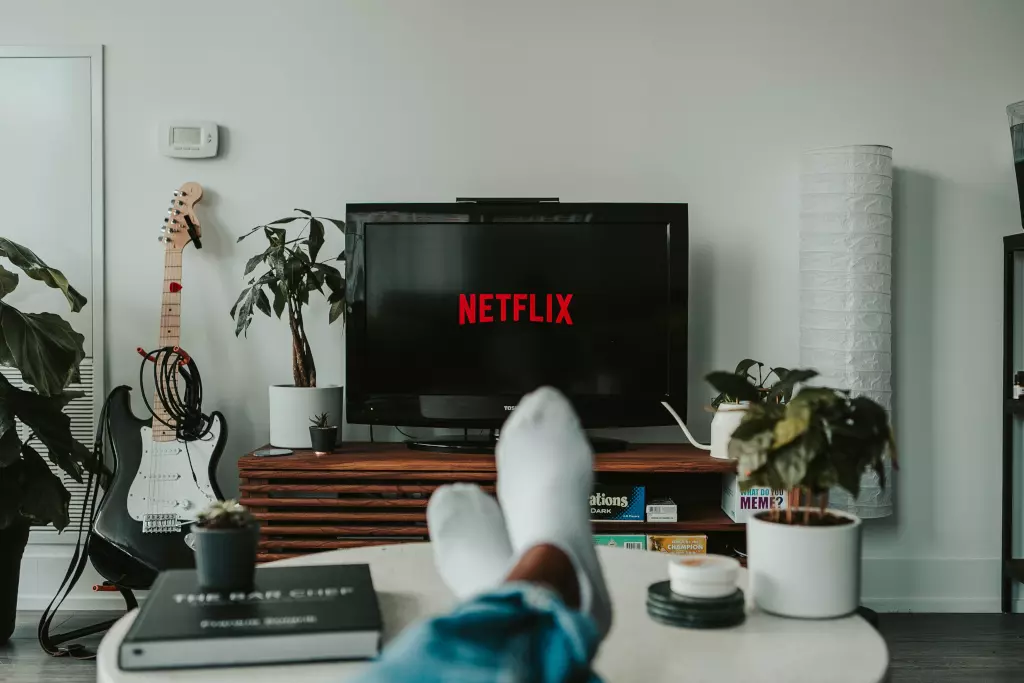 Alguien viendo la plataforma OTT Netflix a través de la aplicación de TV, con un par de flores y una guitarra negra junto al televisor.