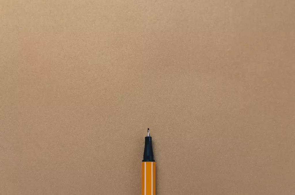 Punta y parte corta de un lápiz naranja con rayas blancas sobre papel reciclado marrón claro