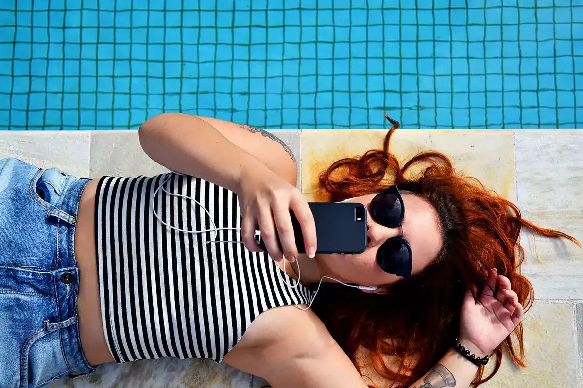 Woman lying on the floor beside a pool engaged in watching streaming content.