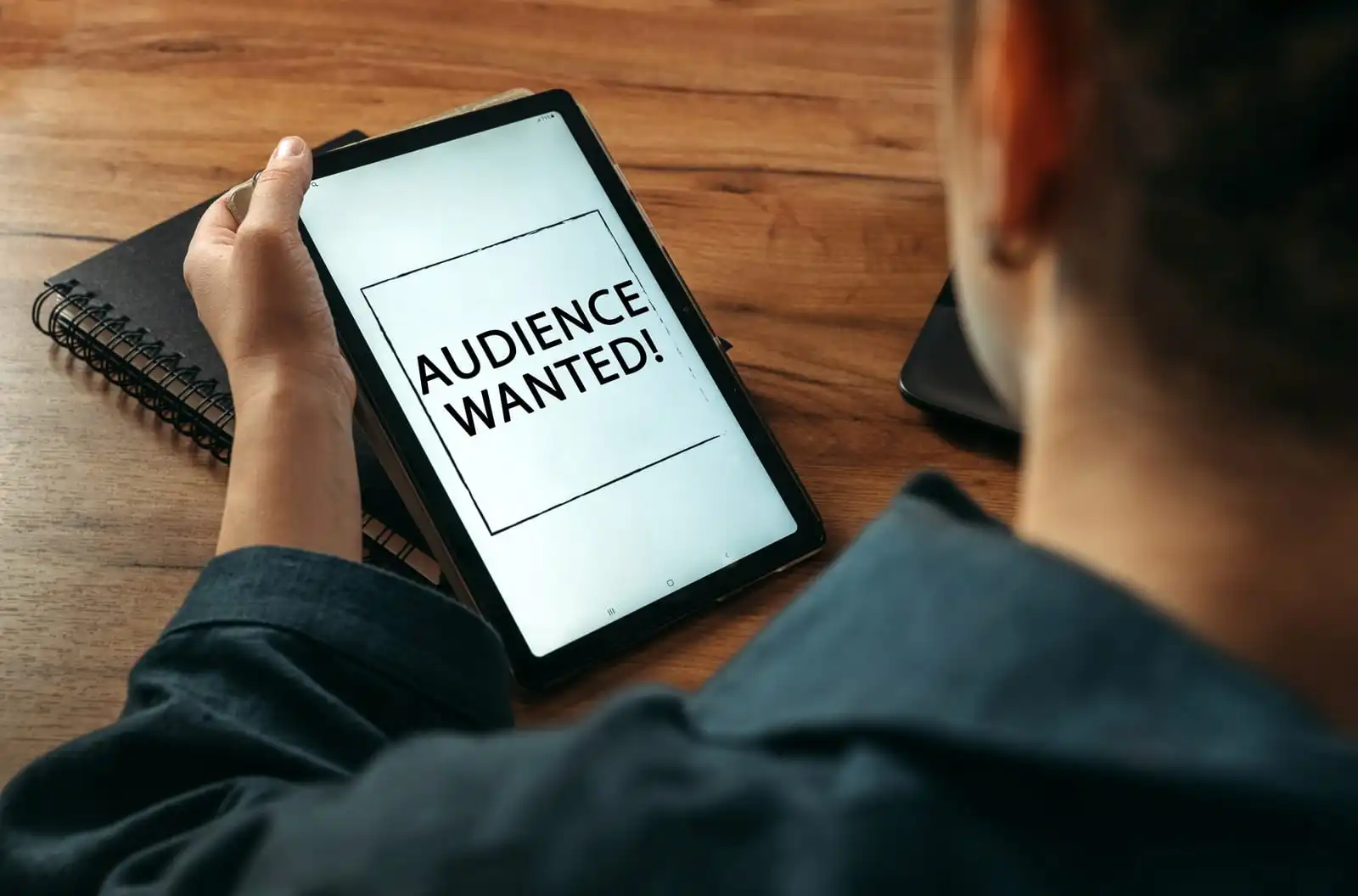Una mujer sostiene una tableta en sus manos, en cuya pantalla está escrito 'Se busca audiencia