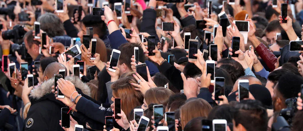 Photo of a crowd of hands holing many smartphones pointed in the same direction