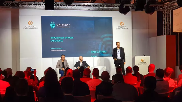 Image showing people watching panel discussion on stage with UniqCast presentation on screen 