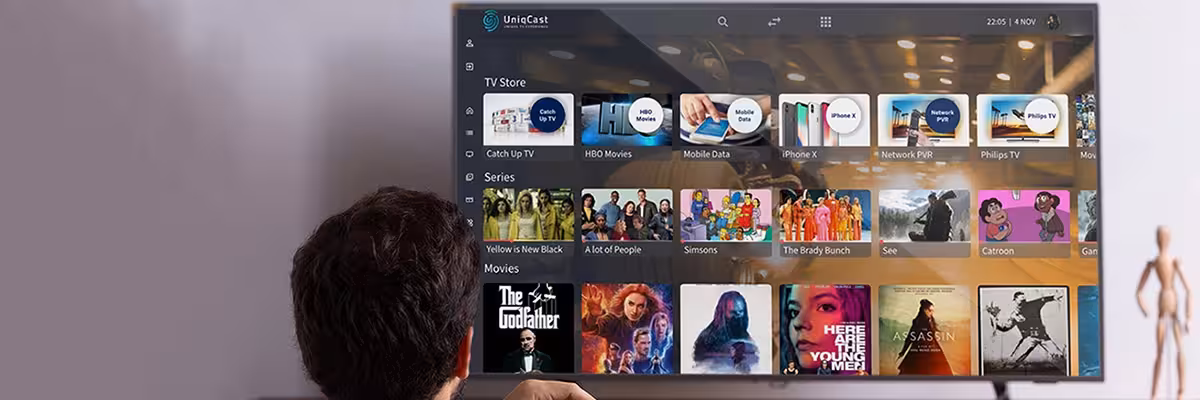 Una persona sostiene un mando a distancia frente a la pantalla de un televisor. La pantalla muestra un menú con varias opciones, que incluyen películas, programas de televisión y datos móviles.